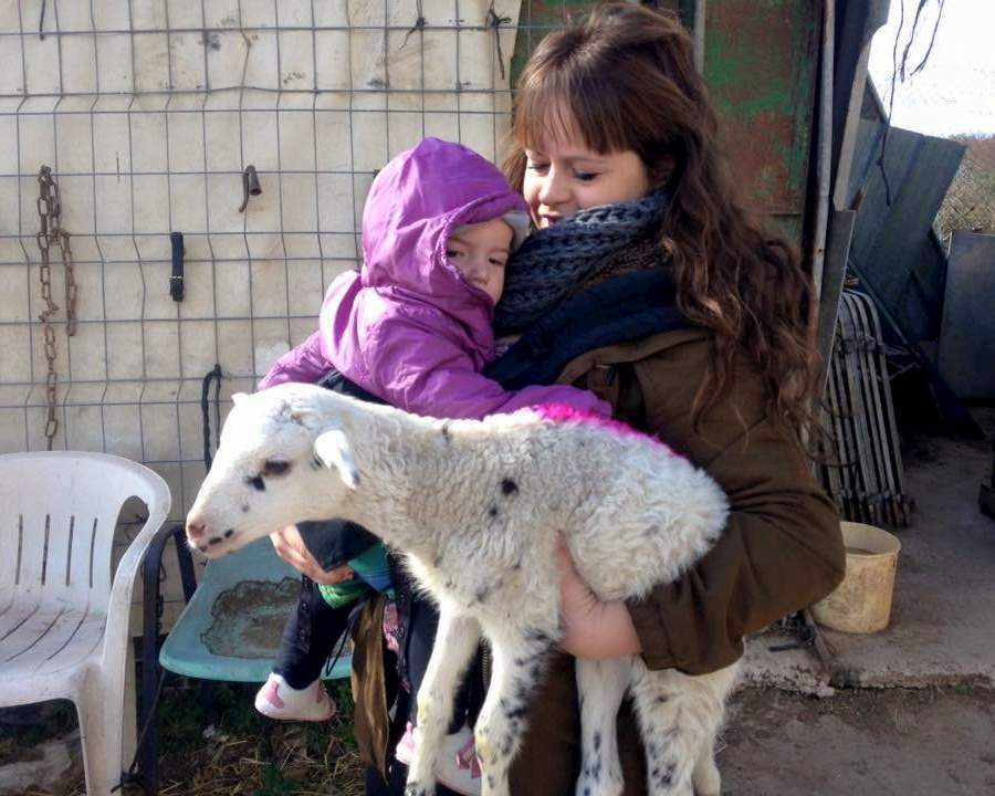 Noia abraçant una nena petita i un xai blanc al refugi